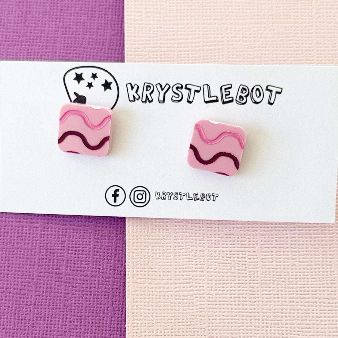 Pink and purple earrings on a card with 'KRYSTLEBOT' branding.