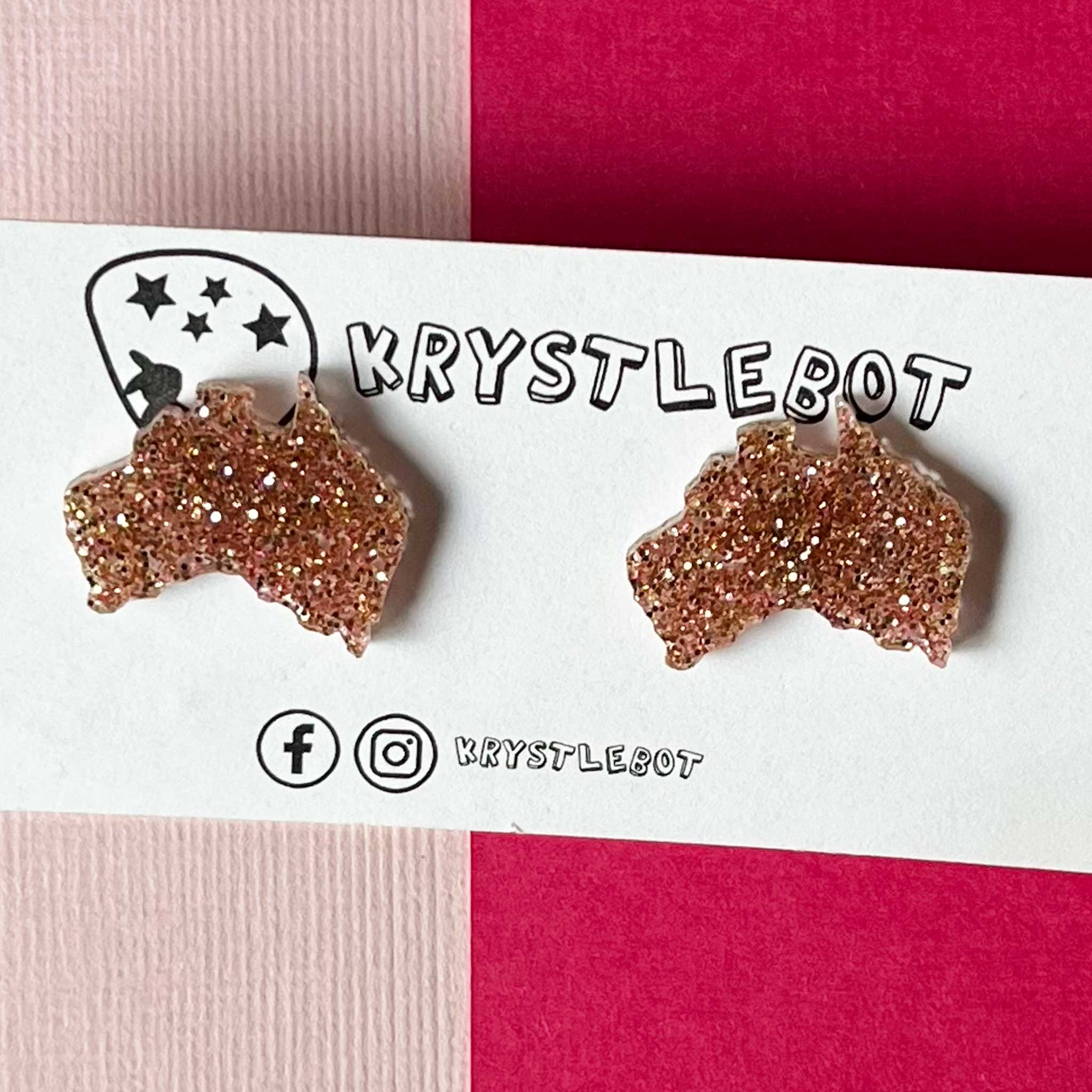Rose gold glittery Australia-shaped earrings on a 'Krystlebot' branded card with pink and white background.
